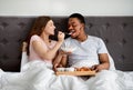 Happy multiracial couple having breakfast in bed, young woman feeding her husband with tasty cereal Royalty Free Stock Photo