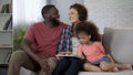 Happy multiracial family planning trip for holidays, booking online on tablet
