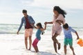 Happy multiracial parents holding hands of children while walking at beach enjoying sunny day Royalty Free Stock Photo