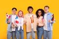 Happy multiracial people holding different countries flags and smiling at camera, standing on yellow background Royalty Free Stock Photo