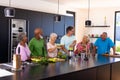 Happy multiracial senior friends talking and making smoothie on kitchen counter at retirement home Royalty Free Stock Photo