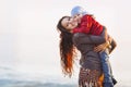 Happy mum and baby girl walking at beach in autumn