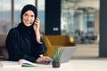 Happy muslim businesswoman in hijab at office workplace. Smiling Arabic woman working on laptop and talking on Royalty Free Stock Photo