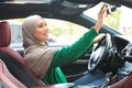 Happy muslim lady driving alone adjusting rearview mirror