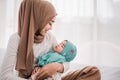 Happy Muslim mother holding adorable little baby daughter wearing hijab in her arms in bedroom. Royalty Free Stock Photo