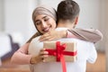 Happy Muslim Wife Hugging Husband Receiving Wrapped Gift At Home