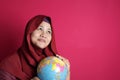 Happy muslim woman wearing red hijab thinking while holding earth globe map on her hand, vacation plan concept Royalty Free Stock Photo