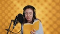 Happy narrator wearing headphones reading aloud from book into mic