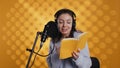 Happy narrator wearing headphones reading aloud from book into mic