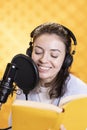 Happy narrator wearing headphones reading aloud from book into mic