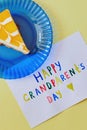 Happy National Grandparents day. Colored greeting card made by children and piece of cake on blue plate as gift