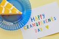 Happy National Grandparents day. Colored greeting card made by children and piece of cake on blue plate as gift