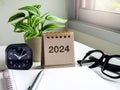 024 numbers year on brown desk calendar cover standing with clock, note book, pen, glasses and green plant pot. Royalty Free Stock Photo