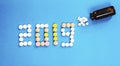 Happy New Year banner for medical theme. Number 2019 made by colored pills/tablets spilling out of brown glass bottle on blue back Royalty Free Stock Photo