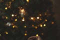 Happy New Year! Burning sparkler in female hand on background of christmas tree lights in dark room. Atmospheric celebration. Hand Royalty Free Stock Photo