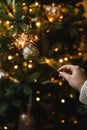 Happy New Year! Burning sparkler in female hand on background of christmas tree lights in dark room. Atmospheric celebration. Hand Royalty Free Stock Photo