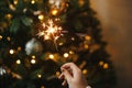 Happy New Year! Burning sparkler in female hand on background of christmas tree lights in dark room. Atmospheric celebration. Hand Royalty Free Stock Photo