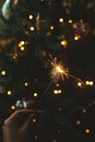 Happy New Year! Burning sparkler in female hand on background of christmas tree lights in dark room. Atmospheric celebration. Hand Royalty Free Stock Photo