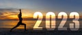 Happy new year card 2023. Silhouette lifestyle woman yoga practicing yoga standing as part of Number 2023 near the beach at sunset