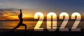 Happy new year card 2022. Silhouette lifestyle woman yoga practicing yoga standing as part of Number 2022 near the beach at sunset Royalty Free Stock Photo