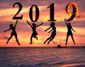 Happy new year card 2019. Silhouette of young woman on the beach jumping as a part of the Number 2019 sign with sunset background Royalty Free Stock Photo