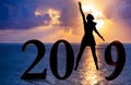 Happy new year card 2019. Silhouette of young woman on the beach stand as a part of the Number 2019 sign with sunset background Royalty Free Stock Photo