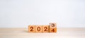 Flipping the 2023 to 2024 year calendar numbers on wooden cube blocks isolated on wood table.