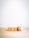Flipping the 2023 to 2024 year calendar numbers on wooden cube blocks isolated on wood table.