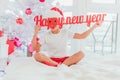 Happy little child, looking like santa, holding a paper text Happy New Year in front of his face near the big Christmas Royalty Free Stock Photo