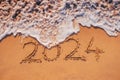Happy New Year 2024 text written on the beach sand and ocean wave washing the sea shore Royalty Free Stock Photo
