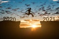 Silhouette of man jump on the cliff between 2020 to 2021 years over sunset or sunrise background.