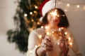 Happy New Year eve party atmosphere. Sparkler burning in hand of stylish girl in santa hat on background of modern christmas tree Royalty Free Stock Photo