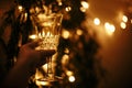 Happy New Year eve party. Hand holding champagne glass on background of golden christmas tree lights, celebrating and toasting in Royalty Free Stock Photo