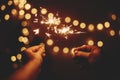 Happy New Year. Glowing sparklers in hands on background of golden christmas tree lights, couple celebrating in dark festive room Royalty Free Stock Photo