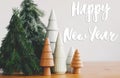 Happy New Year Greeting card. Happy New Year text handwritten on christmas trees on rustic wooden table, small winter forest. Royalty Free Stock Photo
