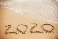 Happy New Year 2020, handwritten on sandy beach. 2020 numbers inscription on golden sand and waves foam at sea beach. Tropical Royalty Free Stock Photo