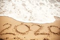 Happy New Year 2020, handwritten on sandy beach. 2020 numbers inscription on golden sand and waves foam at sea beach. Tropical Royalty Free Stock Photo