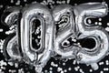 Happy new year 2025 metallic balloons with confetti on dark black background. Greeting card silver foil balloons numbers