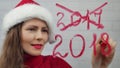 Happy New Year. Santa girl writes lipstick on glass words happy new year. Beautiful girl in hat sending a message.