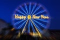Happy New Year sparkling text over a spinning ferris wheel in motion blur against a dark blue sky, copy space Royalty Free Stock Photo