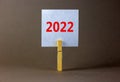 2022 happy new year symbol. Wooden clothespin, white sheet of paper with number 2022. Beautiful grey background, copy space. Royalty Free Stock Photo