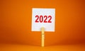 2022 happy new year symbol. Wooden clothespin, white sheet of paper with number 2022. Beautiful orange background, copy space. Royalty Free Stock Photo