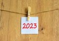 2023 happy new year symbol. Wooden clothespin, white sheet of paper with number 2023. Beautiful wooden background, copy space. Royalty Free Stock Photo