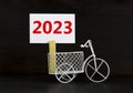 2023 happy new year symbol. Wooden clothespin, white sheet of paper with number 2023. Miniature bicycle model. Beautiful black Royalty Free Stock Photo