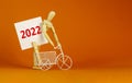 2022 happy new year symbol. Wooden clothespin, white sheet of paper with number 2022. Miniature bicycle model. Beautiful orange Royalty Free Stock Photo