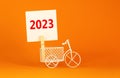 2023 happy new year symbol. Wooden clothespin, white sheet of paper with number 2023. Miniature bicycle model. Beautiful orange Royalty Free Stock Photo