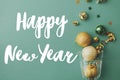Happy New Year text sign on christmas gold baubles and confetti pouring from champagne glass on green background flat lay. Season Royalty Free Stock Photo