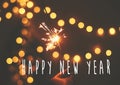 Happy New Year text sign on glowing sparkler in hand on background of golden christmas tree lights in dark festive room. Fireworks Royalty Free Stock Photo