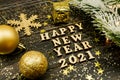 Happy new year 2021 text on wooden background surrounded golden christmas toys and fur tree branch. Festive greeting catd for