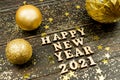 Happy new year 2021 text on wooden background surrounded golden christmas toys and fur tree branch. Festive greeting catd for